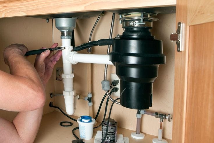 Plumber installing a garbage disposal beneath a kitchen sink in Altamonte Springs